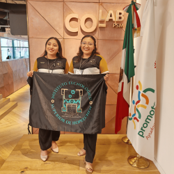 jóvenes ganadoras de El Panalito, posando en el vestíbulo de 'CO-LAB PSM'. Ambas sostienen una lona con el logotipo del "Instituto Tecnológico Superior de Hopelchén" y lucen sonrientes y orgullosas de sus logros. La bandera mexicana y la bandera de Promotora Social México se encuentran a su lado, simbolizando el entorno de colaboración y apoyo para los jóvenes líderes y emprendedores sociales.