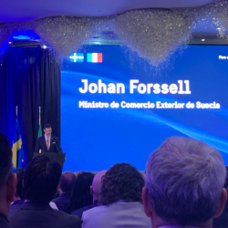 un auditorio con luces azules y brillantina pegada en el techo se encuentra el ministro de comercio exterior de Suecia Johan Forssell en el podium