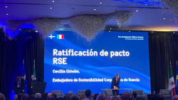 un auditorio con luces azules tres personas en el escenario atrás se puede leer "Ratificación de pacto RSE"